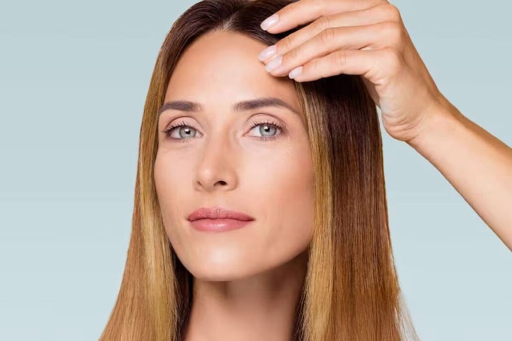 Woman gently lifting her brow, illustrating improved eyelid appearance achievable through blepharoplasty.