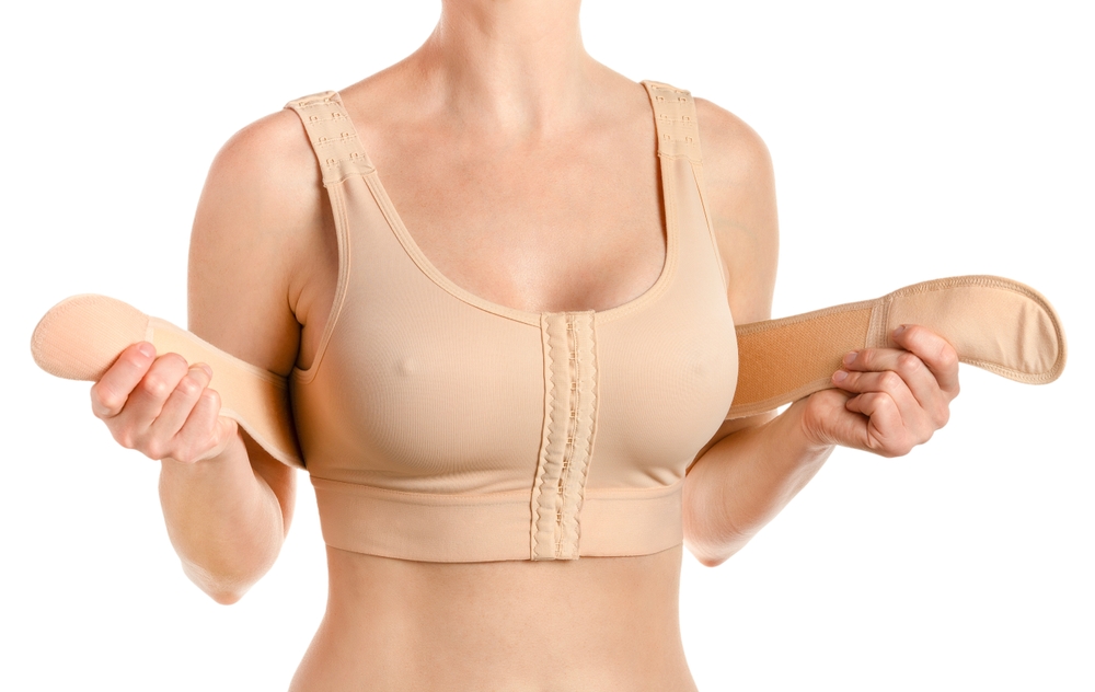Woman wearing and adjusting beige post-surgery compression bra, essential for breast augmentation recovery.