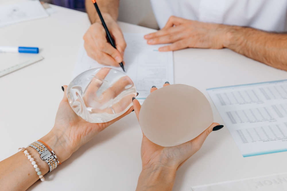 Patient holding two breast implant types while discussing medical history with doctor during breast augmentation consult.
