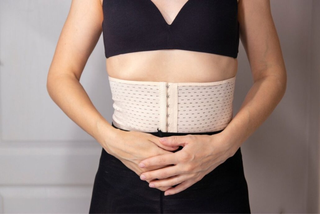 Woman wearing a beige compression garment around her abdomen to support healing after cosmetic surgery.