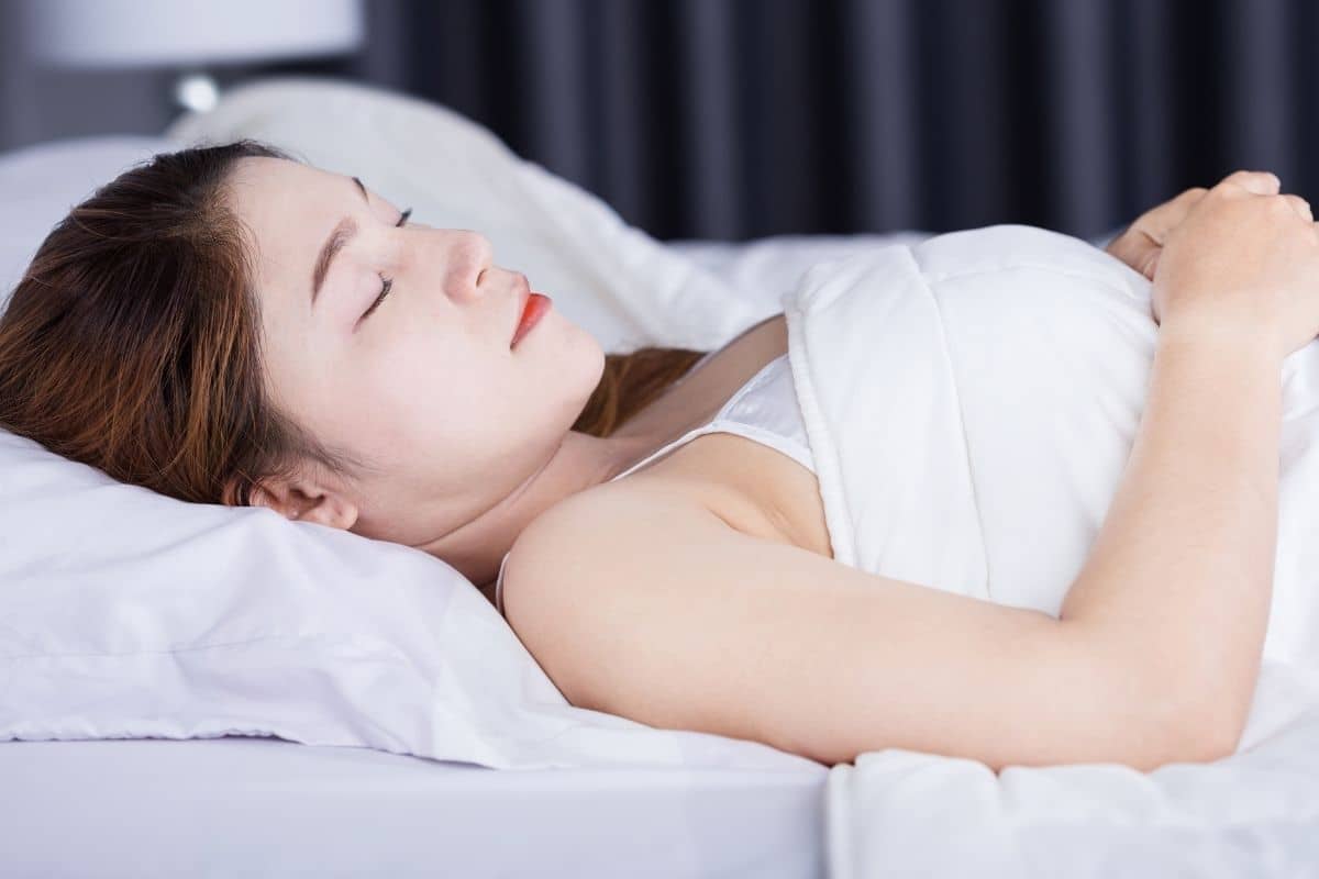 Woman resting on her back in bed, demonstrating ideal sleep position after breast augmentation surgery.